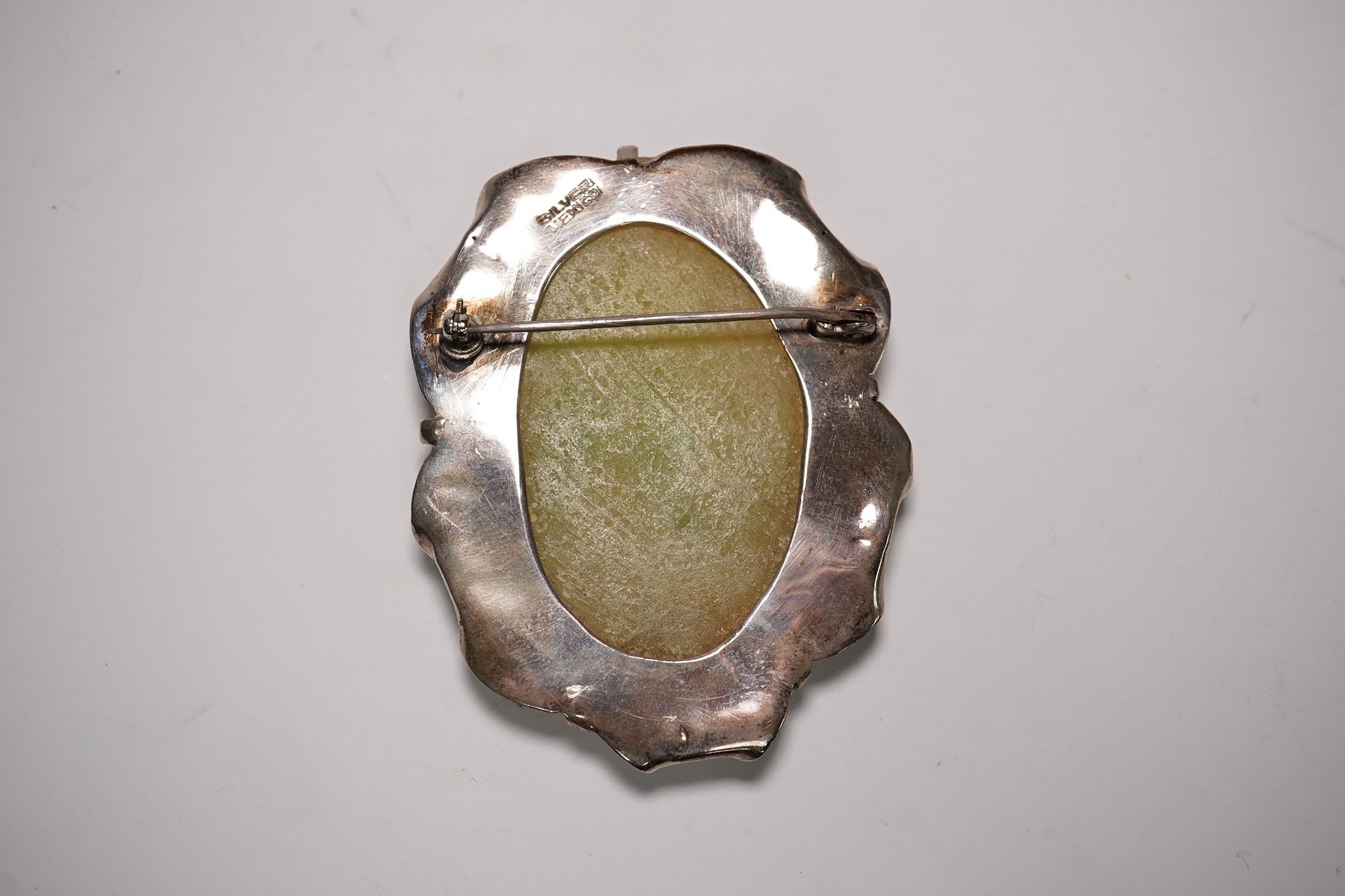 A Mexican silver mounted jadeite brooch, the jadeite face possibly pre-Columbian, 6cm high. Condition - fair, chip to top of brooch